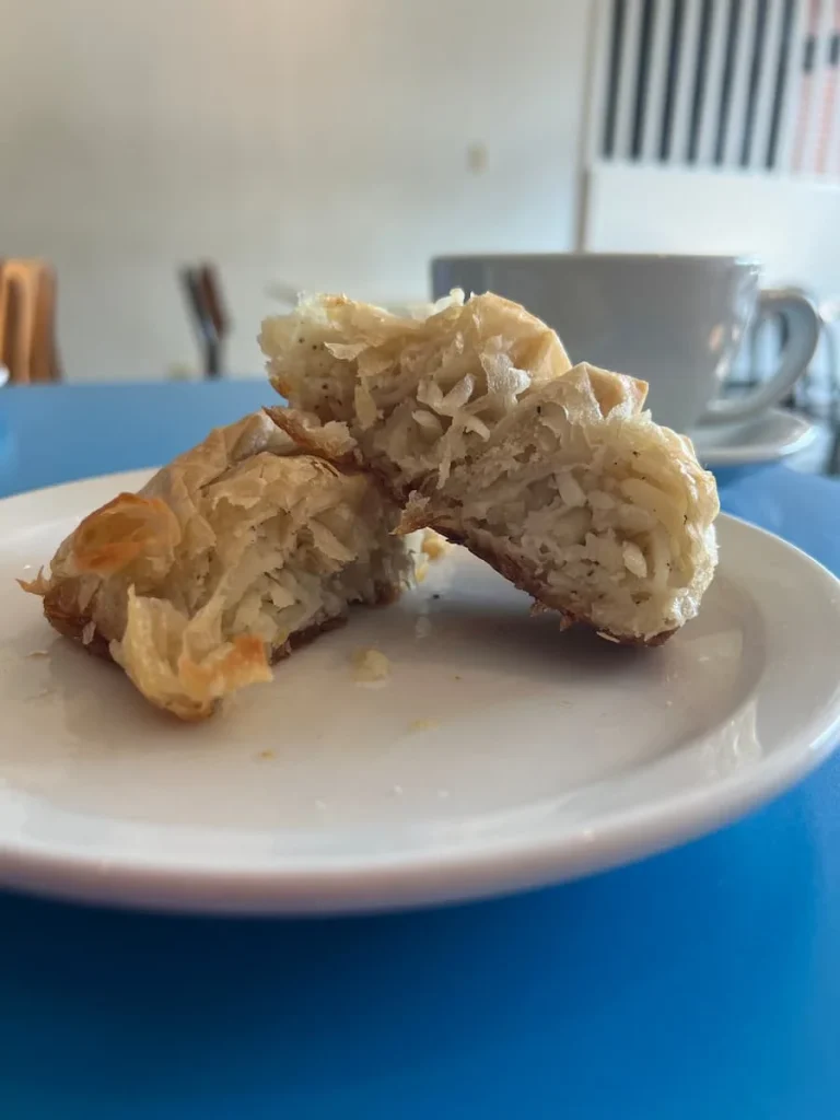A side view of a filo pastry  filled with potato, Burek, Croatian pastry. The pastry has been cut in half to reveal the inner layers of the pastry. The white plate is on a bright blue table top at Doma Cafe, Chicago