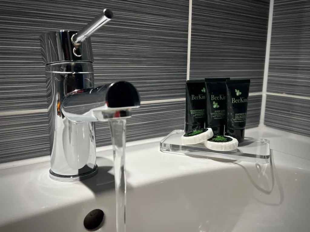 The tap running in the bathroom with Bee Kind toiletteries in the background