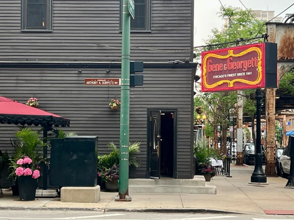 Gene & Georgetti Restaurant sign next to the L tracks in River north with the Anthony Durpetti Street name right outside. The restaurant has a charcoal exterior and outdoor seating in Chicago