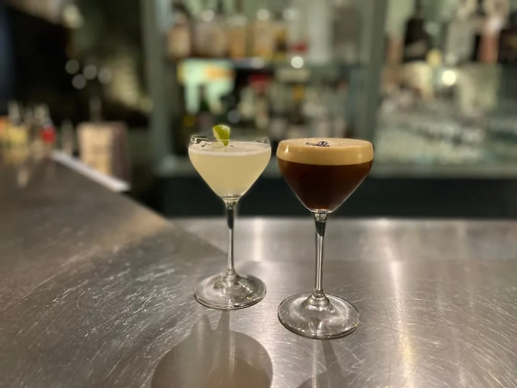 Cocktails at the Q bar at The Queensberry Hotel. One of the cocktails is an Espresso Martini and the other is white with a slice of lime on the rim , both are on the bar top