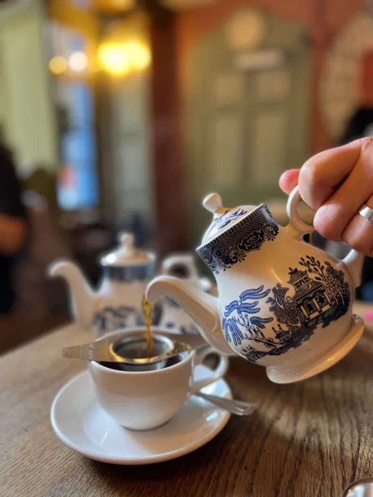 Tea being poured from a white and blue patterned china tea pot through a small sieve at Sally Lunn's Eating House in Bath, England