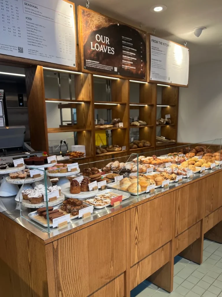 Bakes Counter at Gail's Bakery, Ely. A covered counter with lots of different bakery products inside. The menu is on the wall behind the counter.