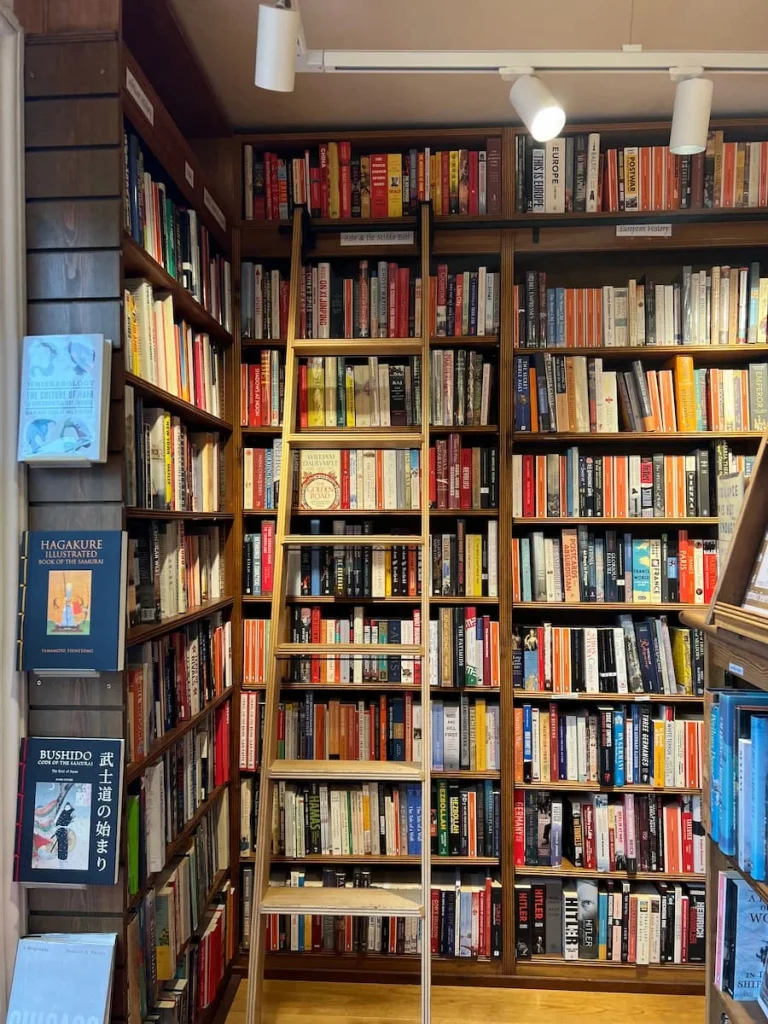 Books on shelves with a ladder against the bookcase at Topping & Co. Ely. The books are multicoloured and lined up neatly in the small room with floor to ceiling bookcases