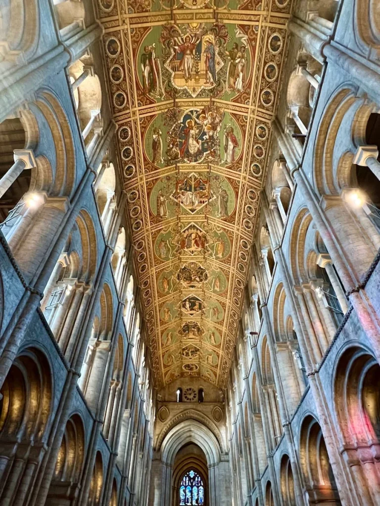 Ceiling in Nave and West Tower of Ely Cathedral. There is intricate painting work on the ceiling with the white stonework arches to the side