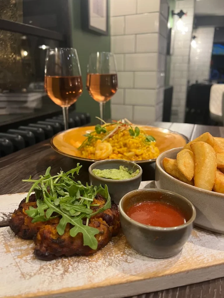 Deconstructed vegetarian burger with paella in the back at Urban Fresh, Ely. The burger is bread less - a patty topped with rocket, a bowl of triple fried chips, guacamole and red salsa
