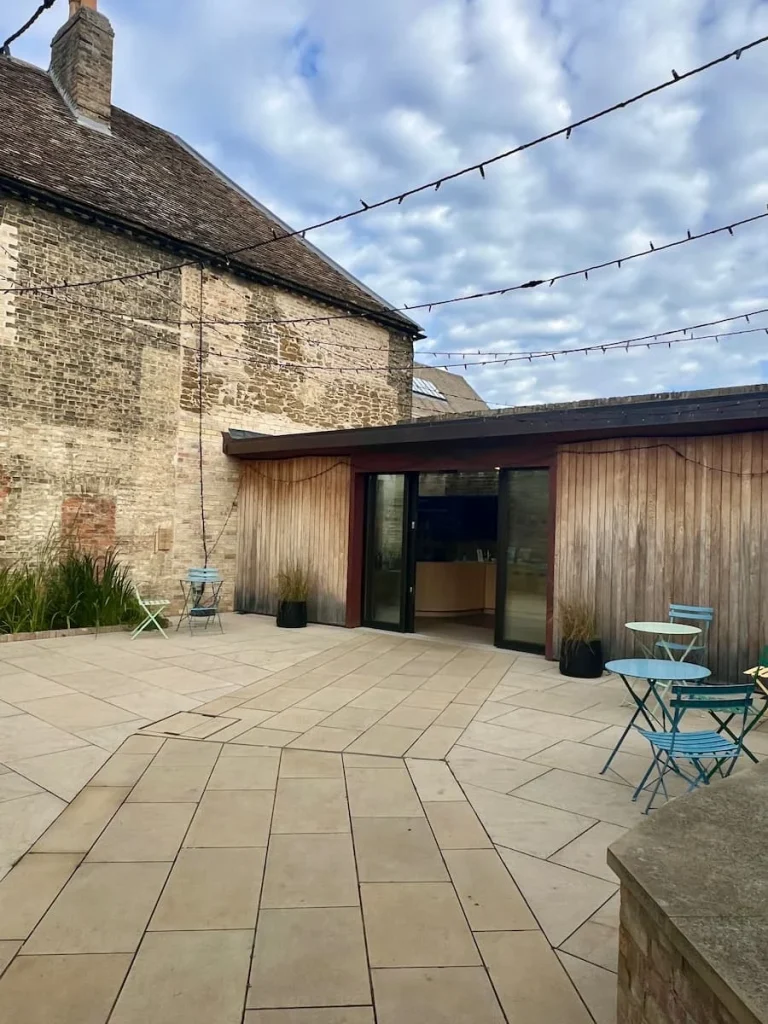 The inner courtyard of Ely Museum with the main museum doors open and pale blue bistro chairs and a table to one side with some small plants at the side too
