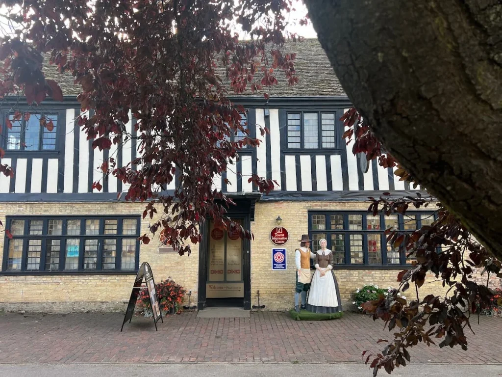 A front on image of the Ely Visitor Centre framed by a tree. There are two mannequins outside resembling 17th century characters wear traditional dress, Ely