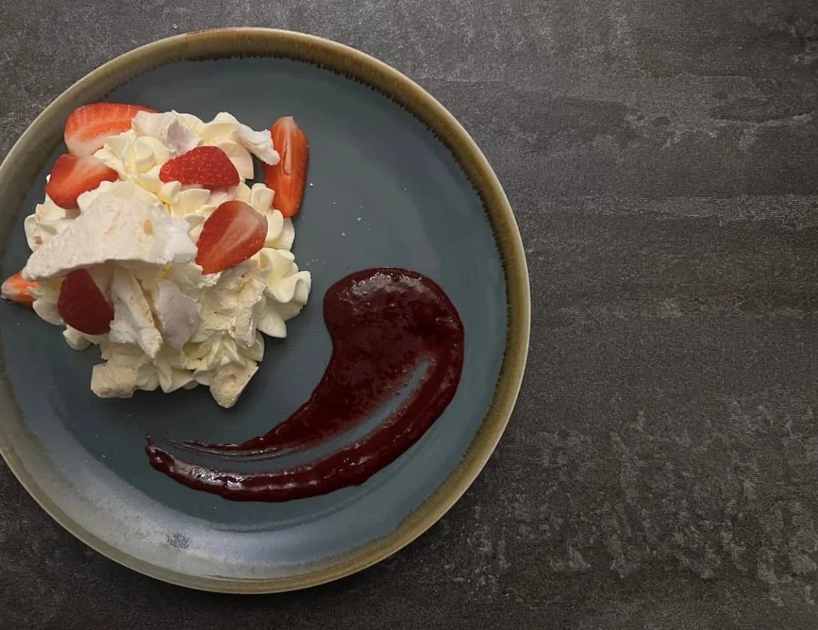 A flat lay of Eton Mess at The Dining Room, Ely. The grey plate with beige rim is on a grey grain grey wood table