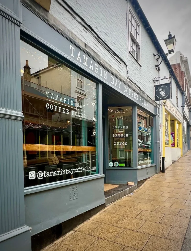 Exterior of Tamarin Bay Coffee House, Ely. The shop is a double-fronted property an dis a dark teal-grey with a shop sign hanging on the outside
