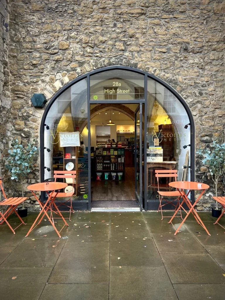Packaged chutneys, crackers adn other offerings at Victoria's Cheese, Ely. The entrance is a semi-circular archway and there are orange bistro tables and chairs outside