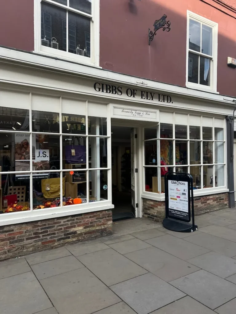 Gibb's of Ely shopfront with shoes in the window. The shop front is double faced with Windows on either side a sandwich board sign outside.