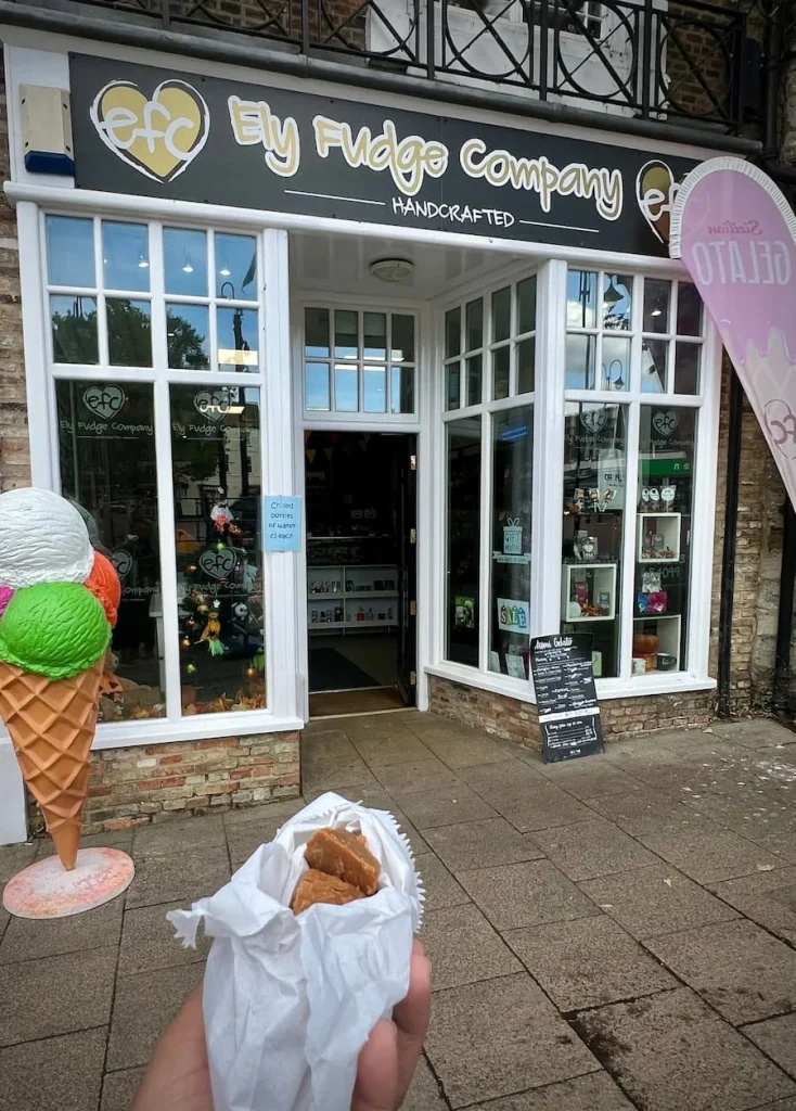 A side view of Ely Fudge Company with bejal holding a white appaer bag with coffee and cream fudge pieces inside