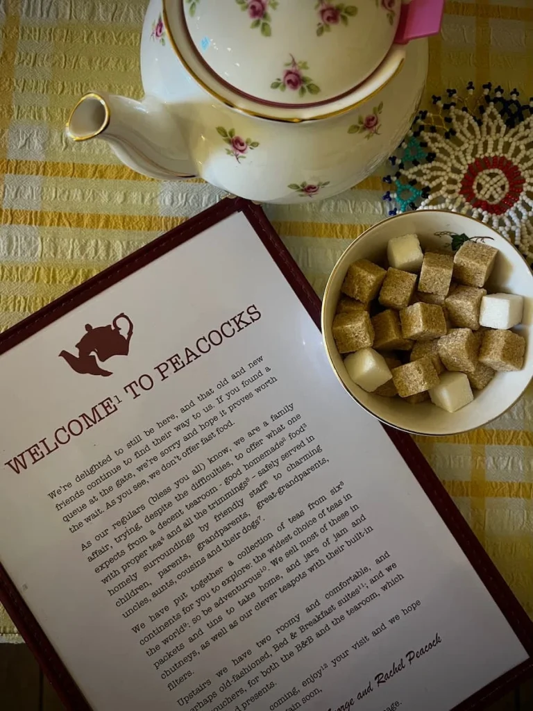 Top lay of the menu at Peacocks Tearoom in Ely. There is a sugar cube bowl and teapot on the table with small flowers.