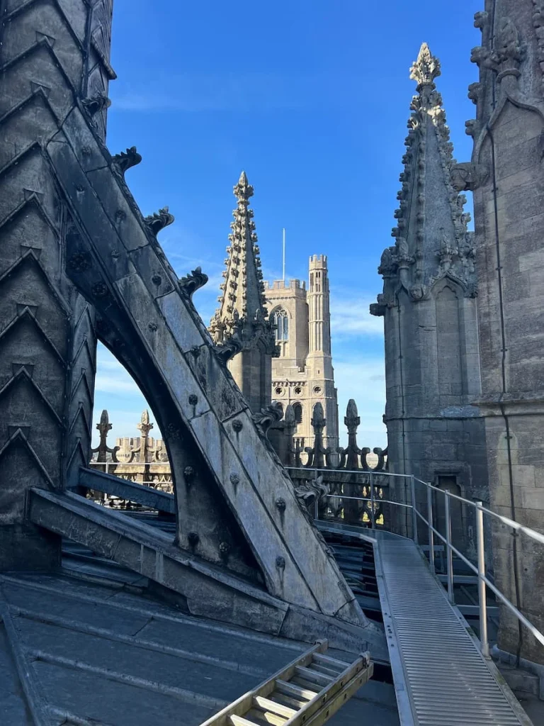 Roof view of the tower at Ely Cathedral. There are structures of the building and a walk way for visitors to walk down close to the main tower on the roof. The structure is in grey