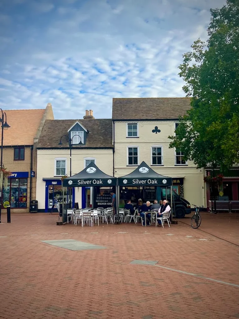Silver Oak Coffee Rig in Market Place, Ely. The Rig is black and white and has tables and seating around it with people chatting and drinking their coffee. One of the vegetarian-friendly places to eat in Ely with their vegan milk options
