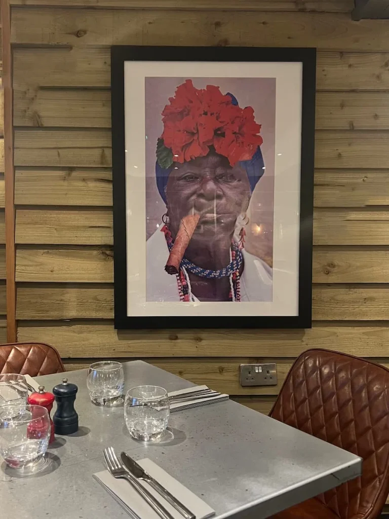 South American lady in photo on wall at Urban Fresh, Ely. The lady is holding a cigar close to her mouth and has red flowers in her hair