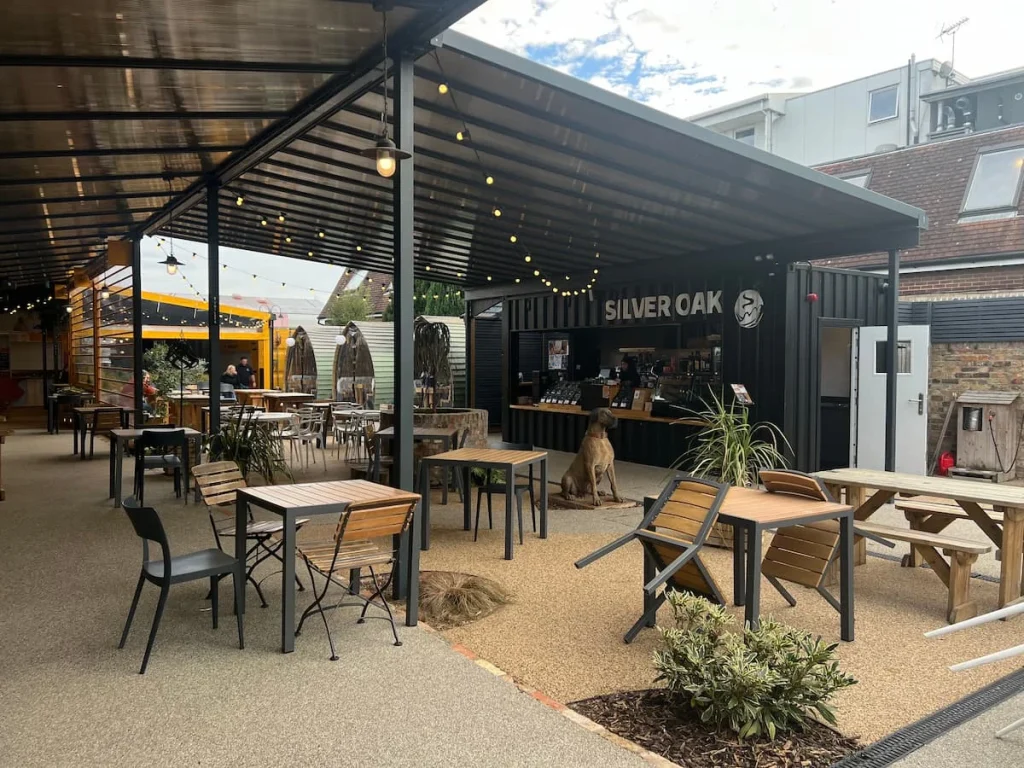 The Yard outdoor seating area with Silver Oak coffee counter, Ely. There are lots of tables and high stools and seats available. The ceiling is covered with fairy lights
