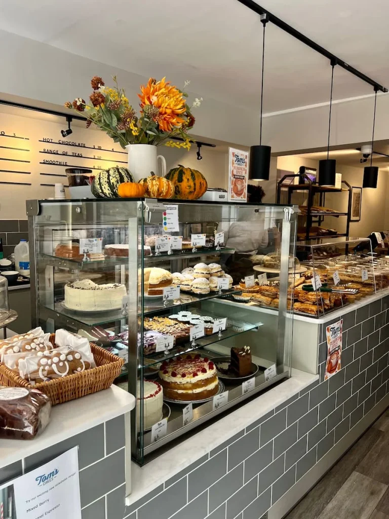 Tom's Cafe counter in Ely with cakes and biscuits laid out inside the covered area at Tom's Cafe in Ely. There are pumpkins on top of teh counter as it was autumn during our visit