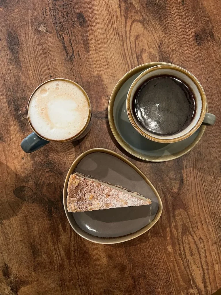 Top lay of chai latte, American coffee and a Victoria Sandwich cake at Tamarin Bay, Ely. They are on a brown grain wooden table