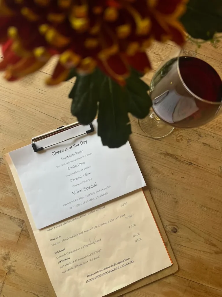 Top lay of red wine and menu at Victoria's Cheese, Ely. They are on a light wood grained table