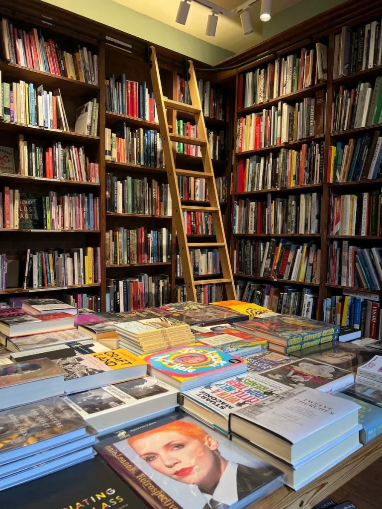 inside at Topping & Company Booksellers of Ely. A room full of floor to ceiling books in lots of colours with a ladder next to the bookcase and a table full of books stacked up