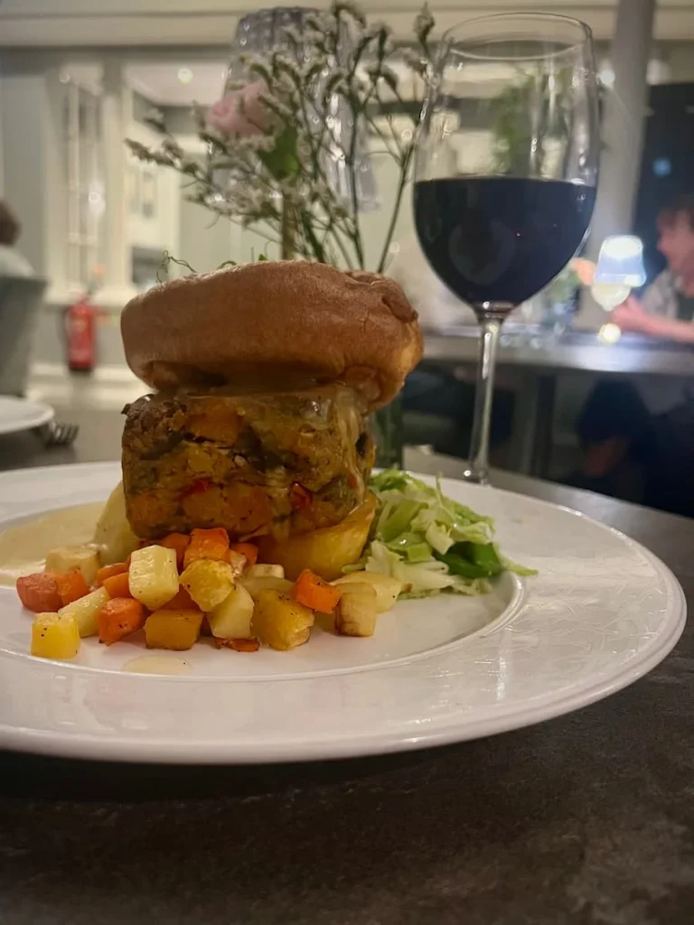 vegetarian Sunday roast at The Dining Room, Ely. The nut roast is topped with seasonal veegatable and a large Yorkshire pudding on top on a white large plate.