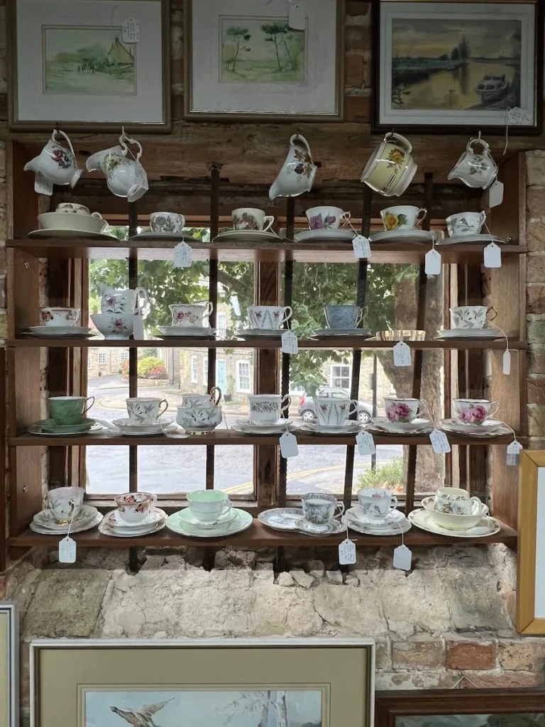 Window with vintage china cups hanging in window of Waterside Antiques. The cups are all white with different colours of florals painted on them