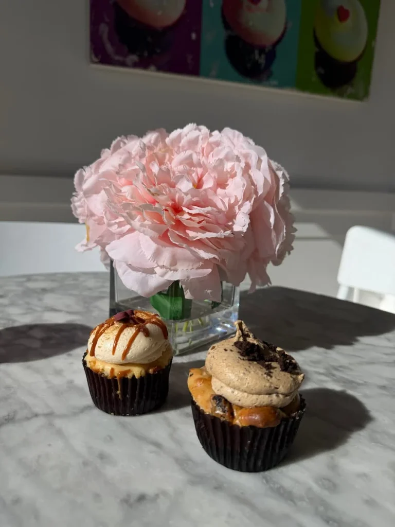 2 cupcakes with pink floral vase at Georgetown Cupcakes, Washington DC, The table is grey marble with the light pouring in and creating shadows