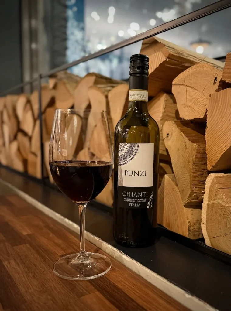 A glass of red wine and bottle of Punzi at Via Sophia, Washington DC. There are cut wooden logs in the background
