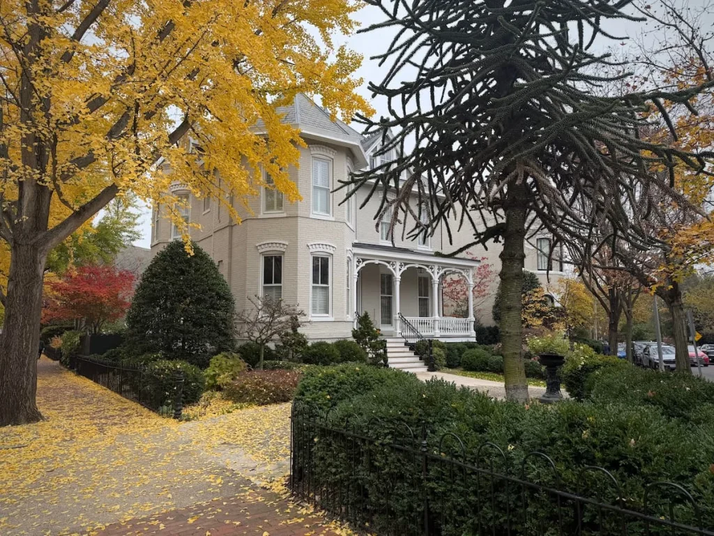 A house in Dumbarton Oaks in Georgetown Washington DC. The houses off white fascia is covered by autumnal trees adn foliage