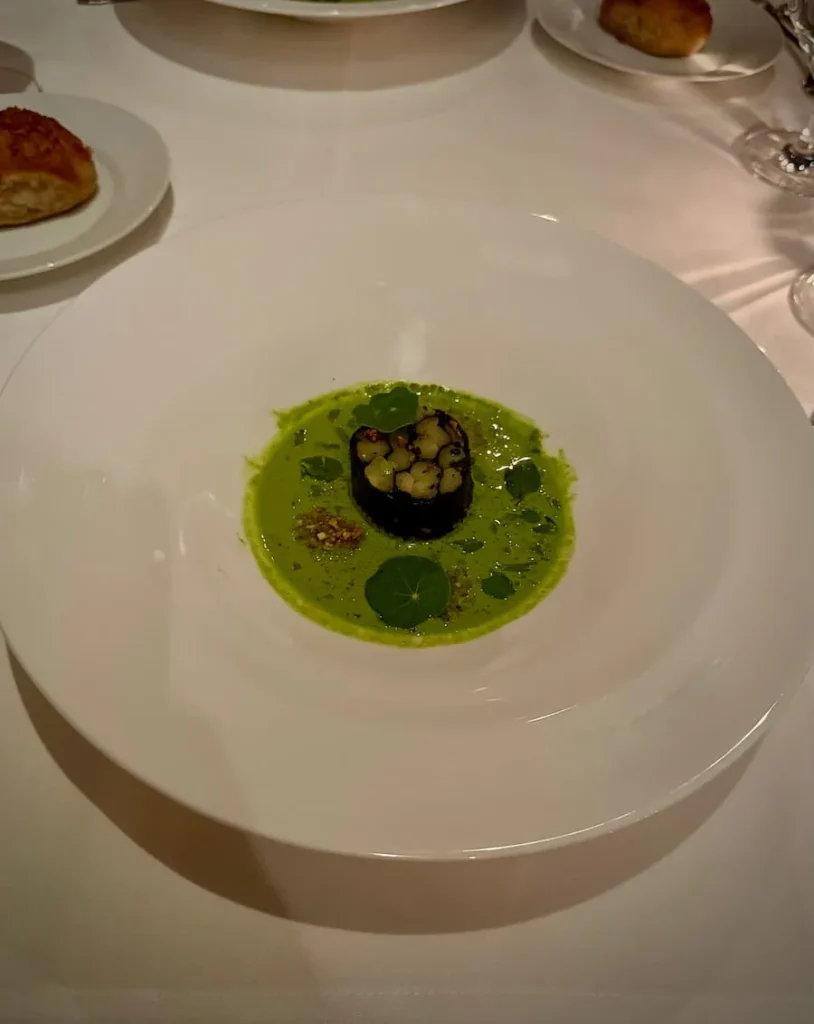 Appetiser at Elizabeths, Washington DC. A large white plate on a white table cloth with poached white asparagus, nori, oyster leaf. There is a peek of the bread in the top left hand corner of the image.