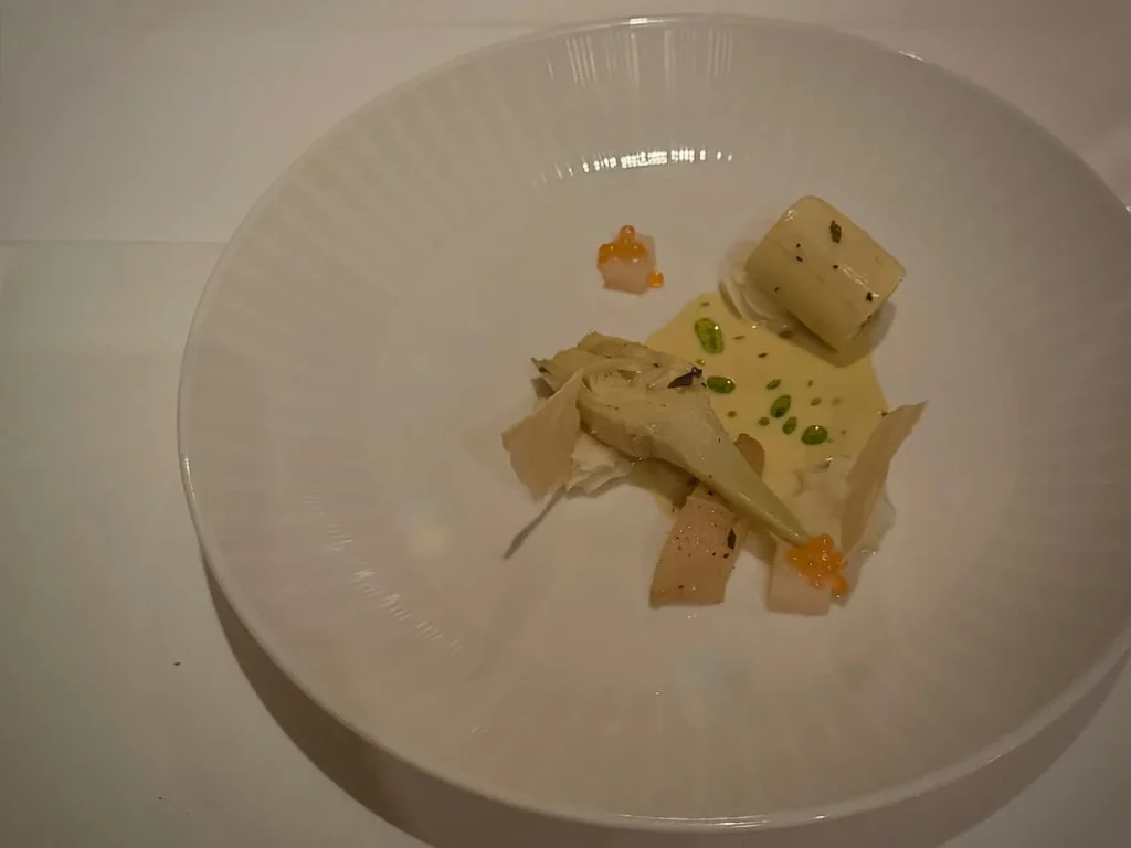 Artichoke Main at Elizabeths, Washington DC. A circular large white plate on the white table cloth with artichoke, grilled heart of palm, cipollini onion hollandaise