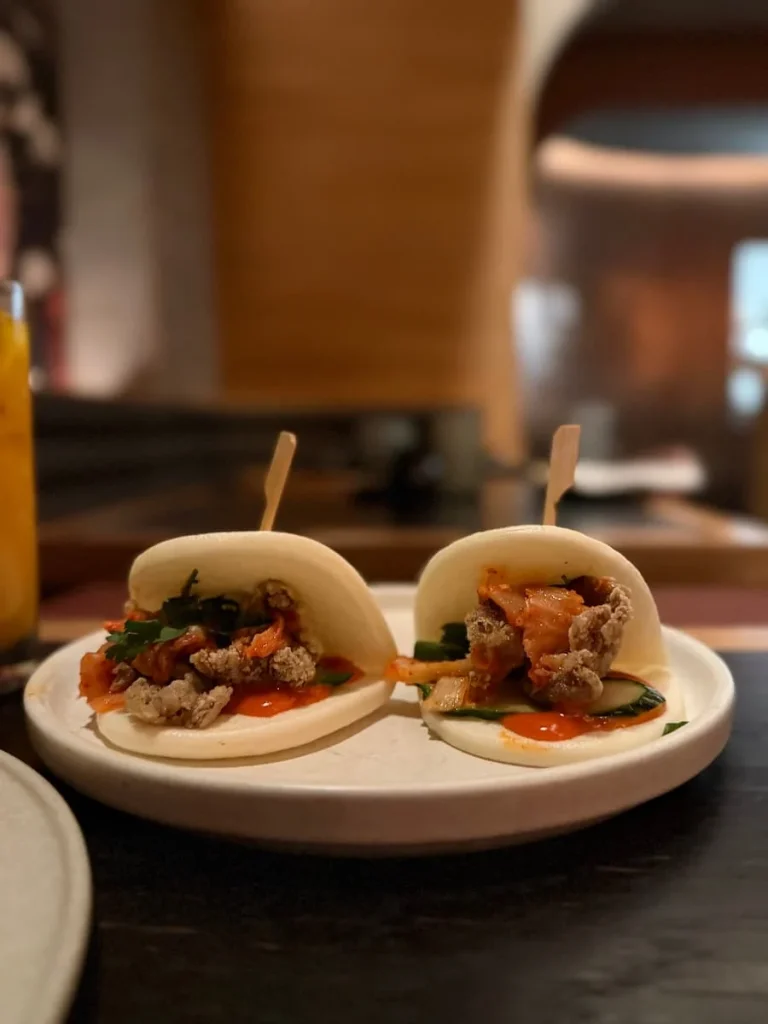 Bao buns at Planta Queen, Washington DC. There are two bao buns filled with mushrooms on a white earthenware plate and a blurred background