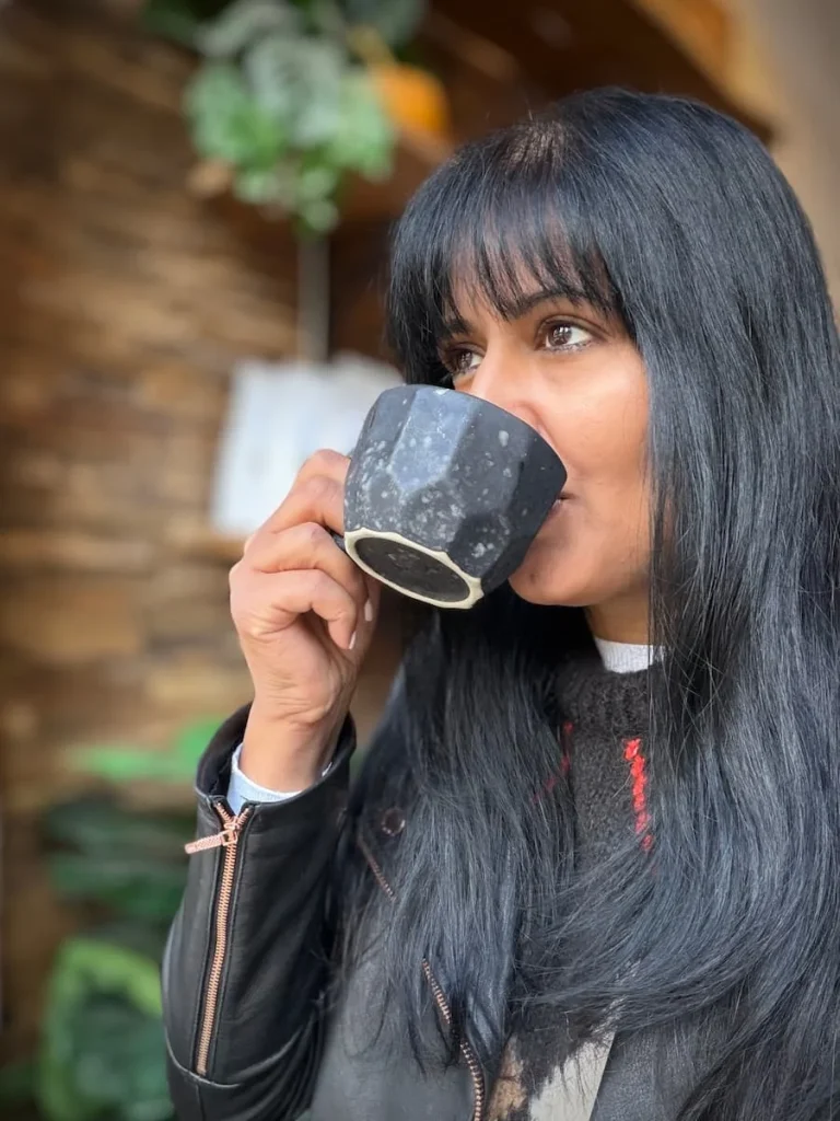 Bejal sipping on coffee at Dua DC Coffee in a dark grey cup with shelving behind her. One of teh vegan and vegetarian places to eat in Washington DC
