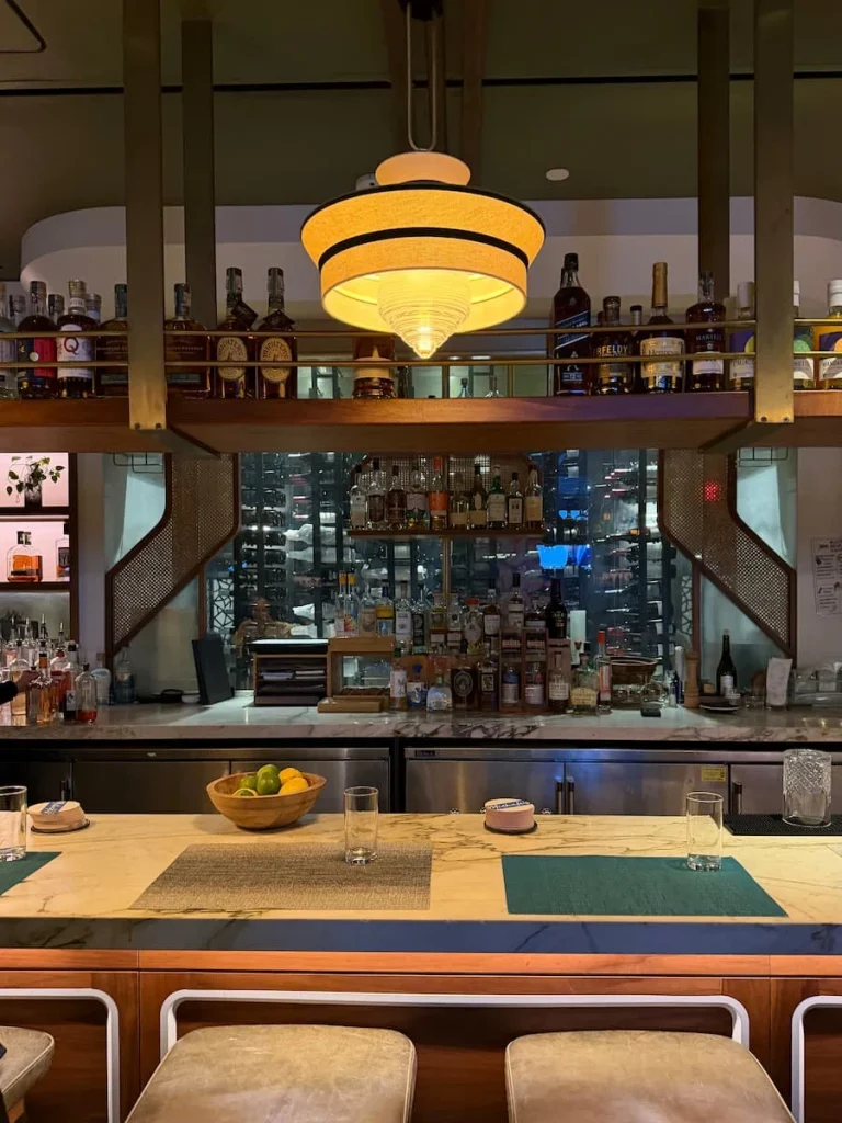 Close-up of Bar at Michele's Washington DC. The area is set uo with place settings, a big light dropping down and spirits in the background that reflect from the large mirror behind the bar.