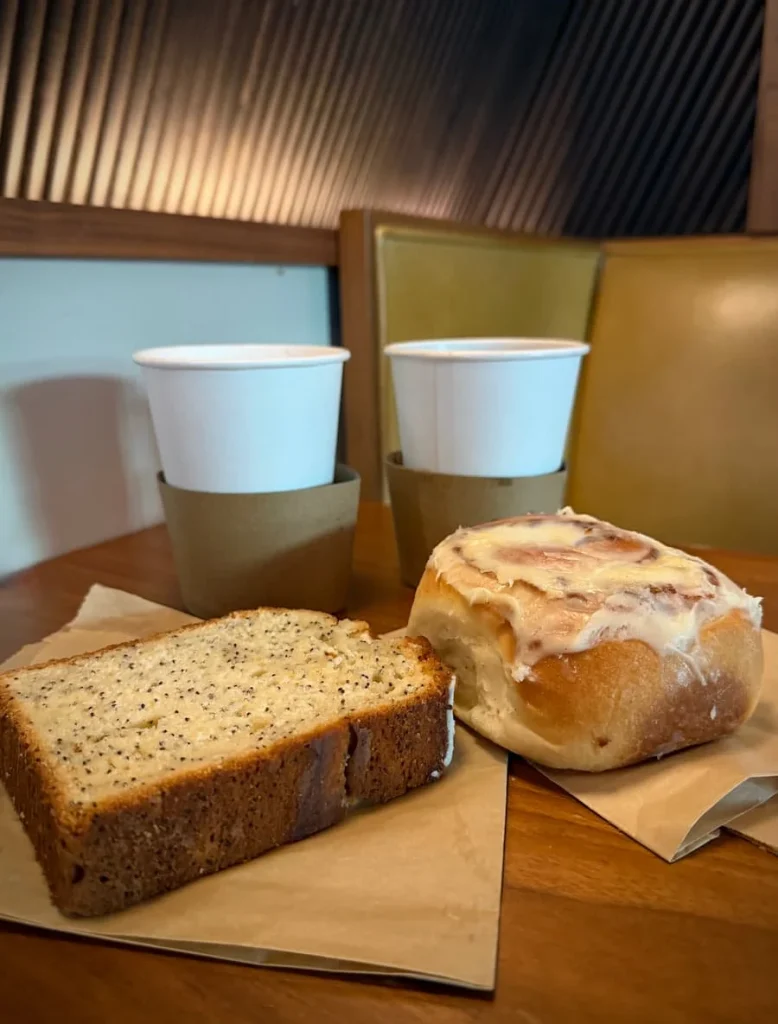 Coffees and cakes at Baker's Daughter, Washington DC. The pastries are lemon and poppy seed bread and the pastry is a danish with cream cheese frosting on a brown wooden table in Washington DC