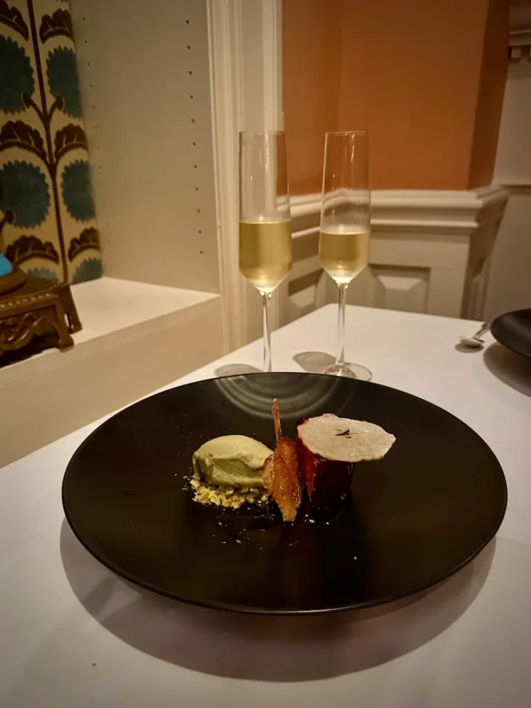 Dessert at Elizabeths, Washington DC. A large black plate with balsamic & strawberry sauce, dark chocolate, pistachio-vanilla gelato. There are two flutes of soarkling wine in the background against the salmon pink wall and blue antique vase.