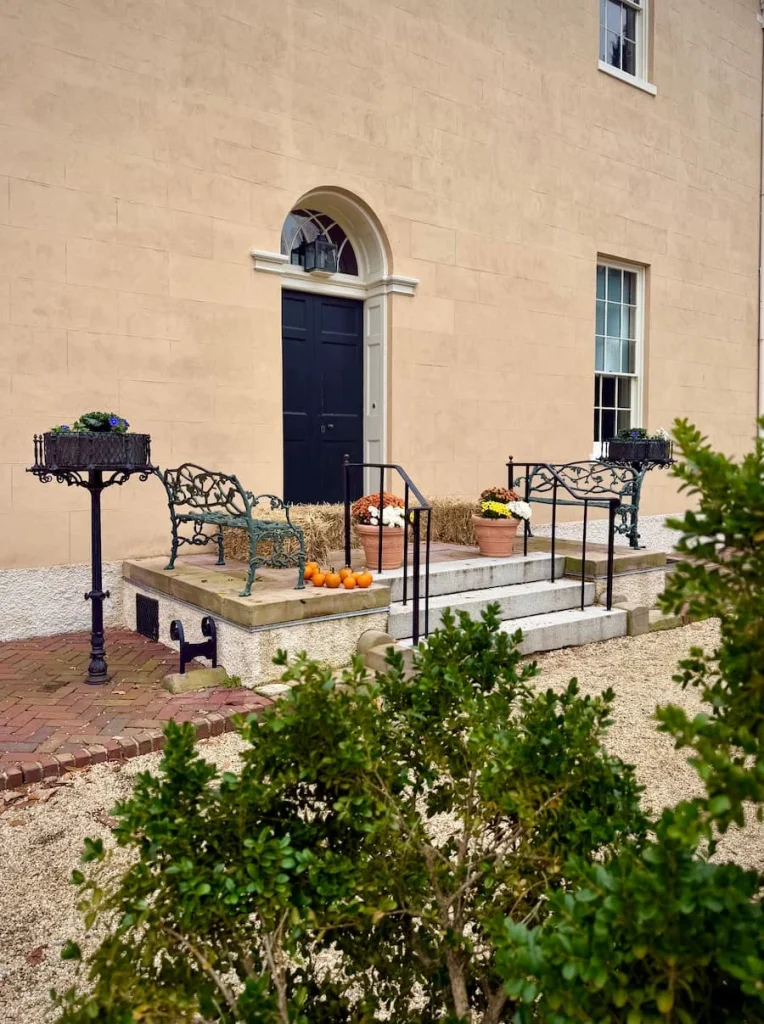 Entrance way with pumpkins at Tudor House in Georgetown Washington DC. The door is black with plants and poted trees at either end 