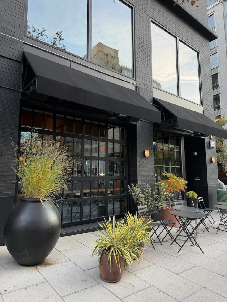 Exterior of Baker's Daughter, Washington DC with black frontage and big black pots with green grass and foliage as well as black bistro chairs and tables