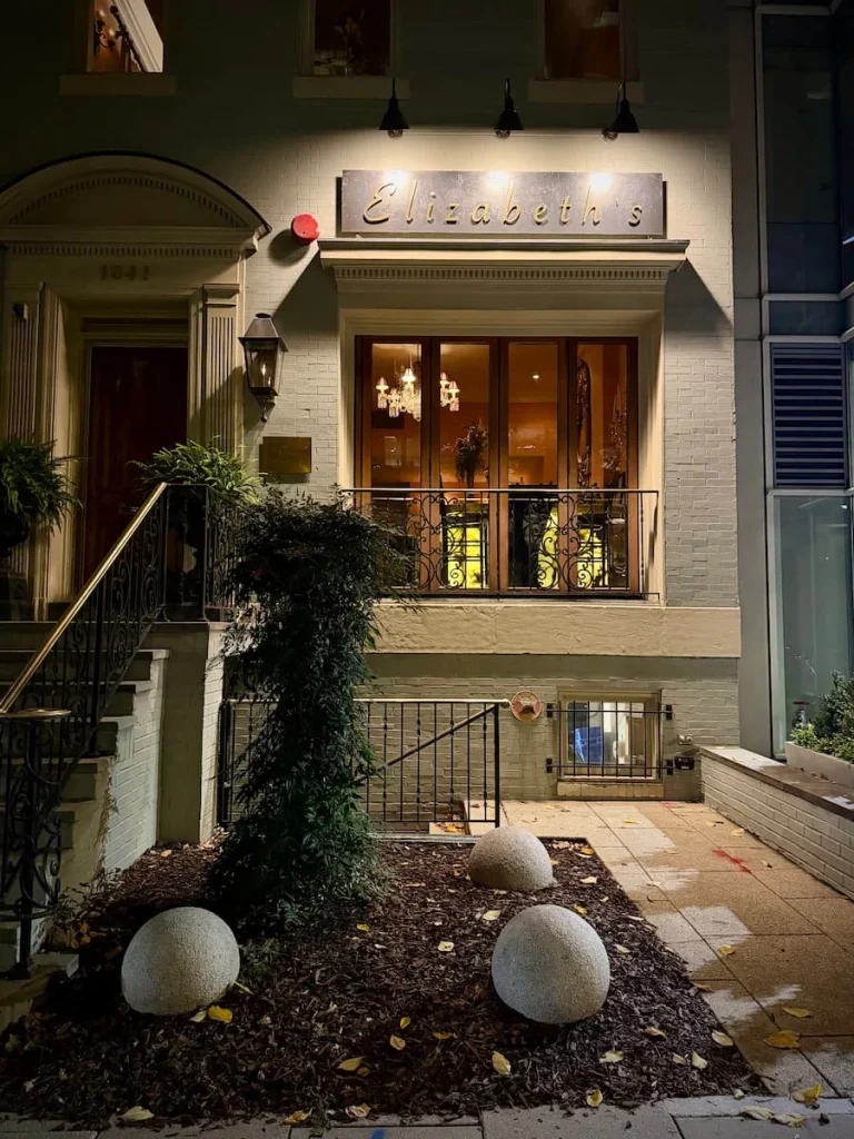 Exterior of Elizabeth's vegan fine dining in  Washington DC, housed in a 3 storey town house. Theer are steps leading up tp the entrance and the front window has teh light on revealing the bar area
