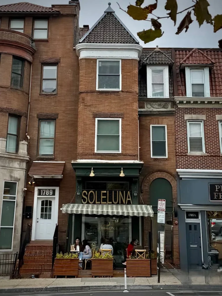 Exterior of Soleluna, Washington DC. The 3 story building with the bakery on the ground floor. The awning covers a small seating area with people sitting and enjoying their goodies.
