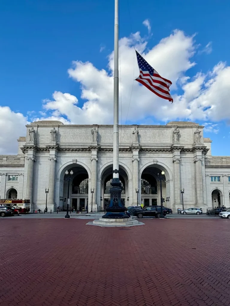 Exterior of Union Station, Washington DC with US flag outside and taxis queuing up for pick-ups outs doe the historical building with 3 white arches. Sustainable things to do in Washington DC