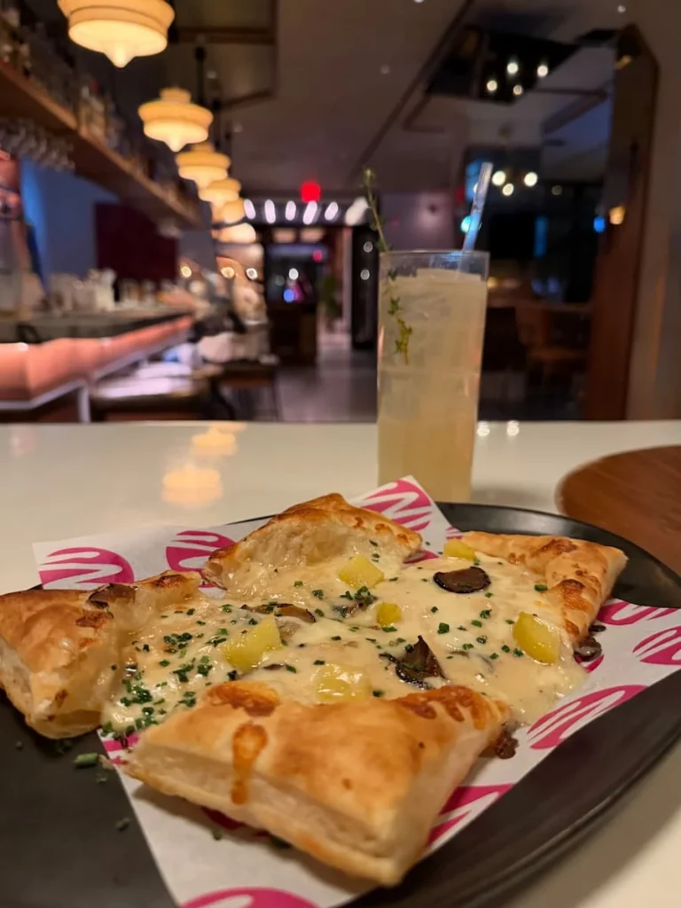 Food and drink at Michele's Washington DC. The a glass of teh non-alcoholic cocktail in the background of the shop with the bar and a truffle and cheese puff pastry tarte on a white table top