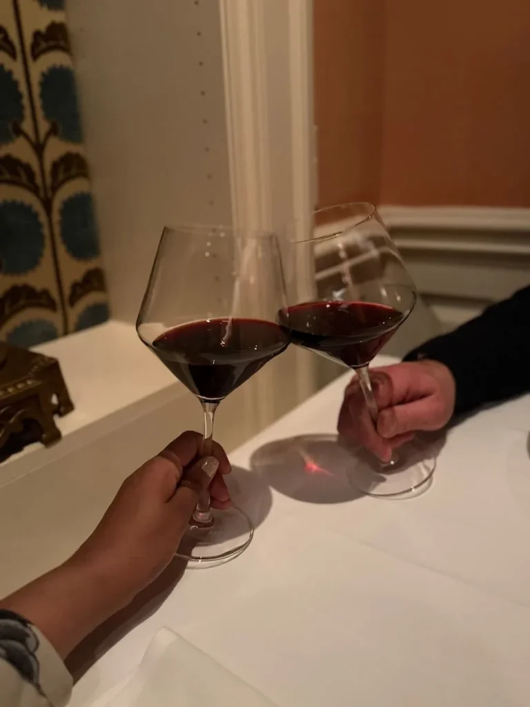 Gelsomoro Red Wine at Elizabeths, Washington DC. Bejal and Will doing a cheers with a glass of red wine each with the salmon pink background in the back and blue ornate vase to the left of the image