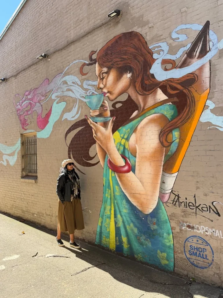 Just Paper & Tea Mural in Georgetown, Washington DC. A girl is sipping on tea in a blue tea cup with Bejal standing next to the mural