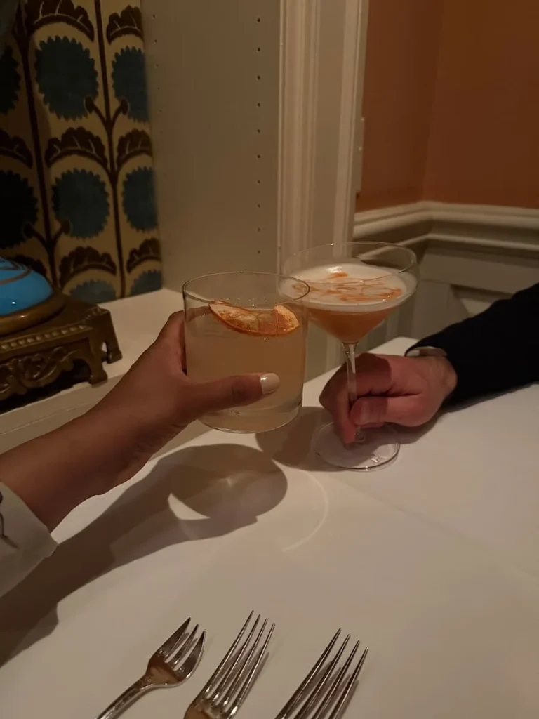 Bejal and Will doing a cheers with a Hemingway in Havana and Amaretto ginger Sour at Elizabeths, Washington DC under a white table cloth.