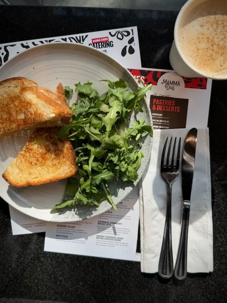 A flat lay of a honey lavender latte in a paper cup and a signature grilled cheese with rocket salad at Mamma Dos, Washington DC