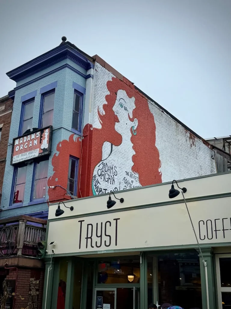 Madams Organ street art, of a lady with orange hair next to the wall of Tryst coffee in Washington DC. Adams Morgan has a few sustainable hotels in Washington DC
