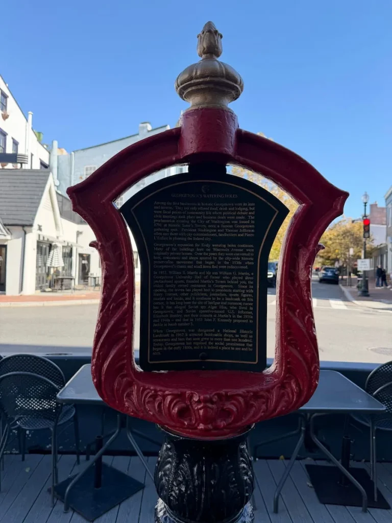 Martin's Tavern historic Plaque outside the restaurant in Georgetown, Washington DC with gold writing on a black background and a red frame. The street can be seen in the background