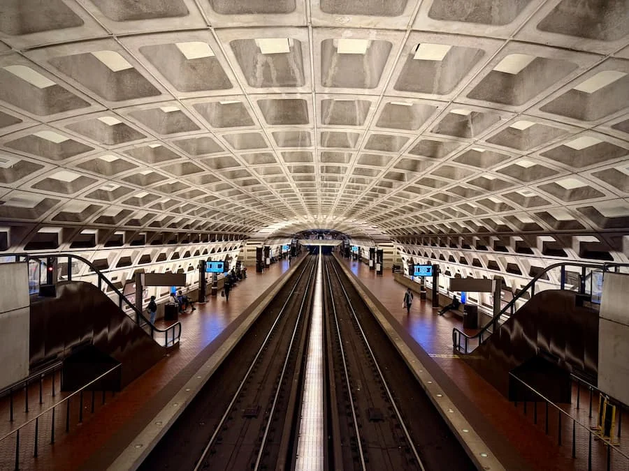 Metro Center Station, Washington DC with people on either side and an ornate ceiling with train tracks in the middle